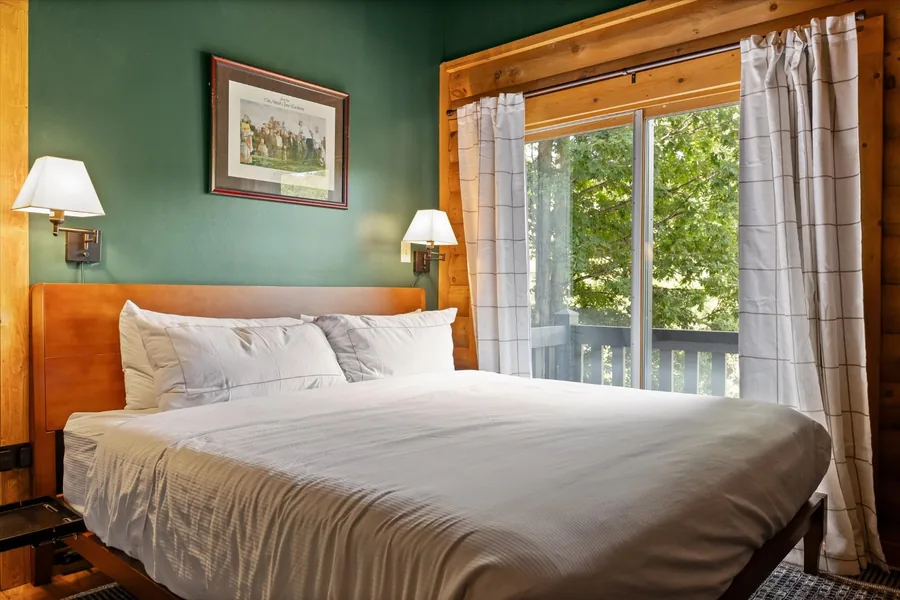 King bedroom with green walls, log detail and a window to the deck