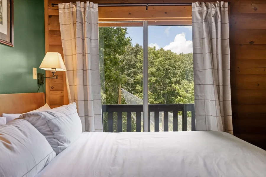 King bedroom with the deck door curtains drawn open to the hardwoods