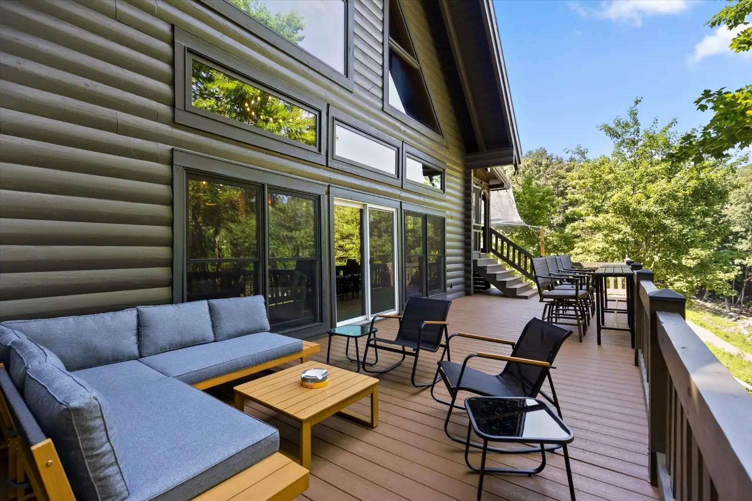 Outdoor sectional and coffee table on a wide deck with the tree line beyond