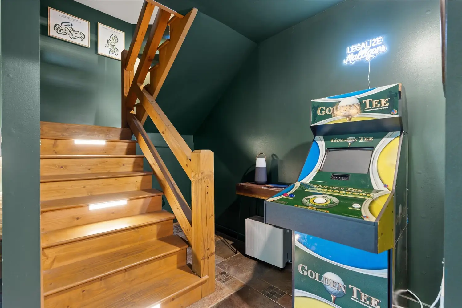 Golden Tee arcade cabinet lit up beside a wooden staircase