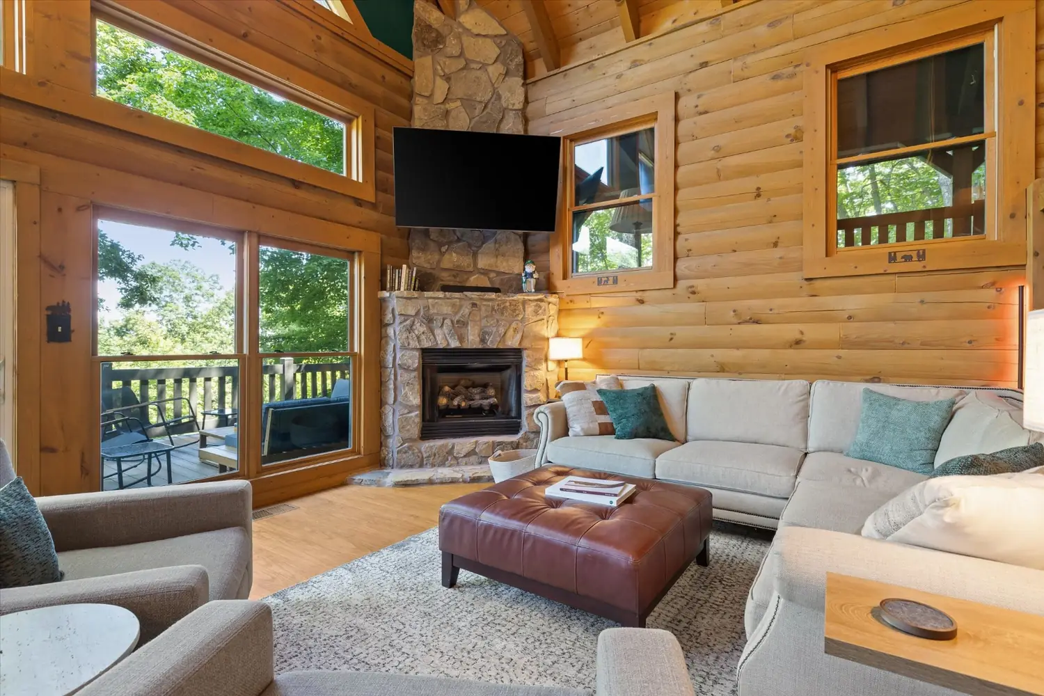 Great room with a sectional sofa, stone fireplace and a wall of windows under vaulted log beams