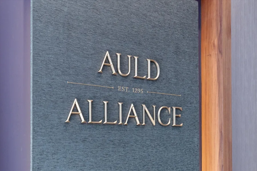 Auld Alliance lettering carved into a slate panel beside a wood door