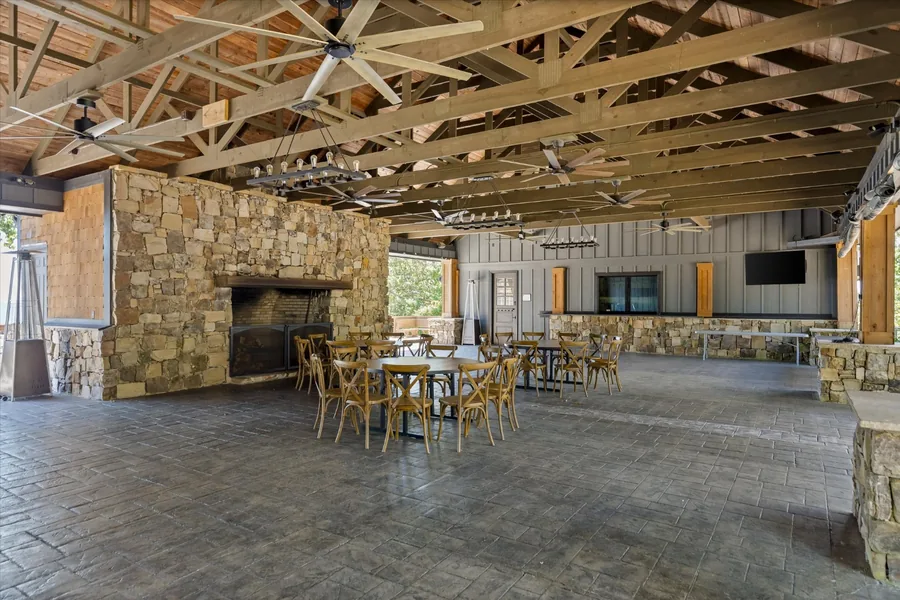 Open-air pavilion interior with a stone fireplace, long tables and ceiling fans