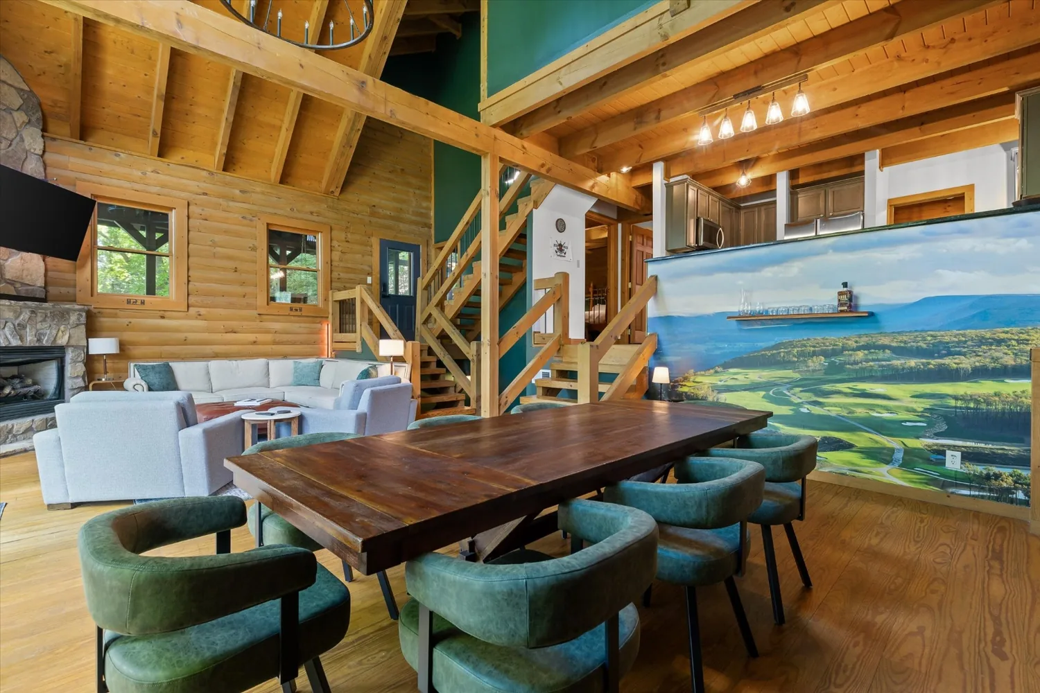 Walnut dining table and green chairs in front of the floor-to-ceiling mural of The Keep, open to the great room and the log staircase