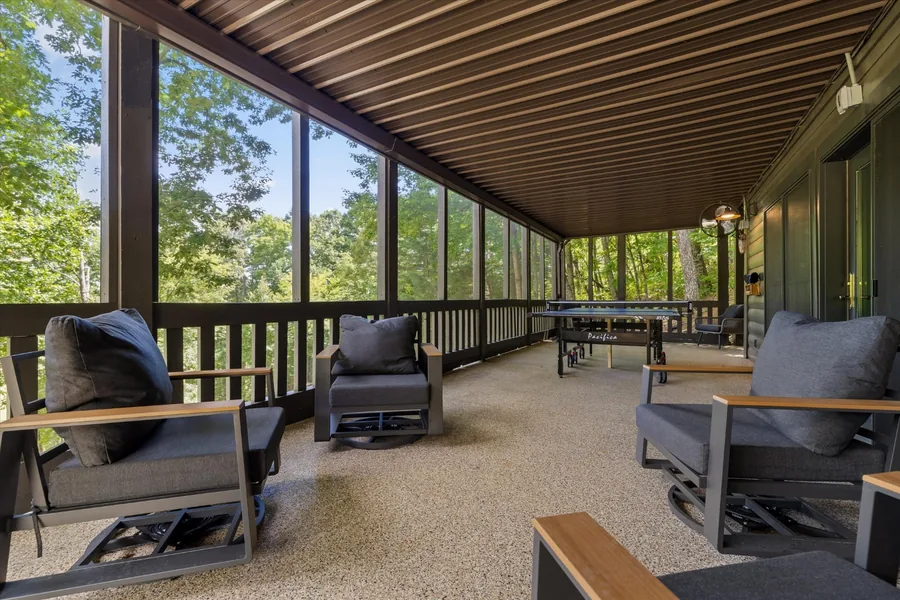 Long screened porch with lounge chairs and the woods beyond